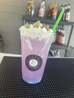 A purple dirty soda topped with whipped cream and candy